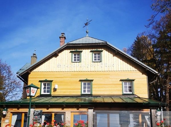 Dřevěná chata se zelenými okenicemi a větrolamem na střeše.
