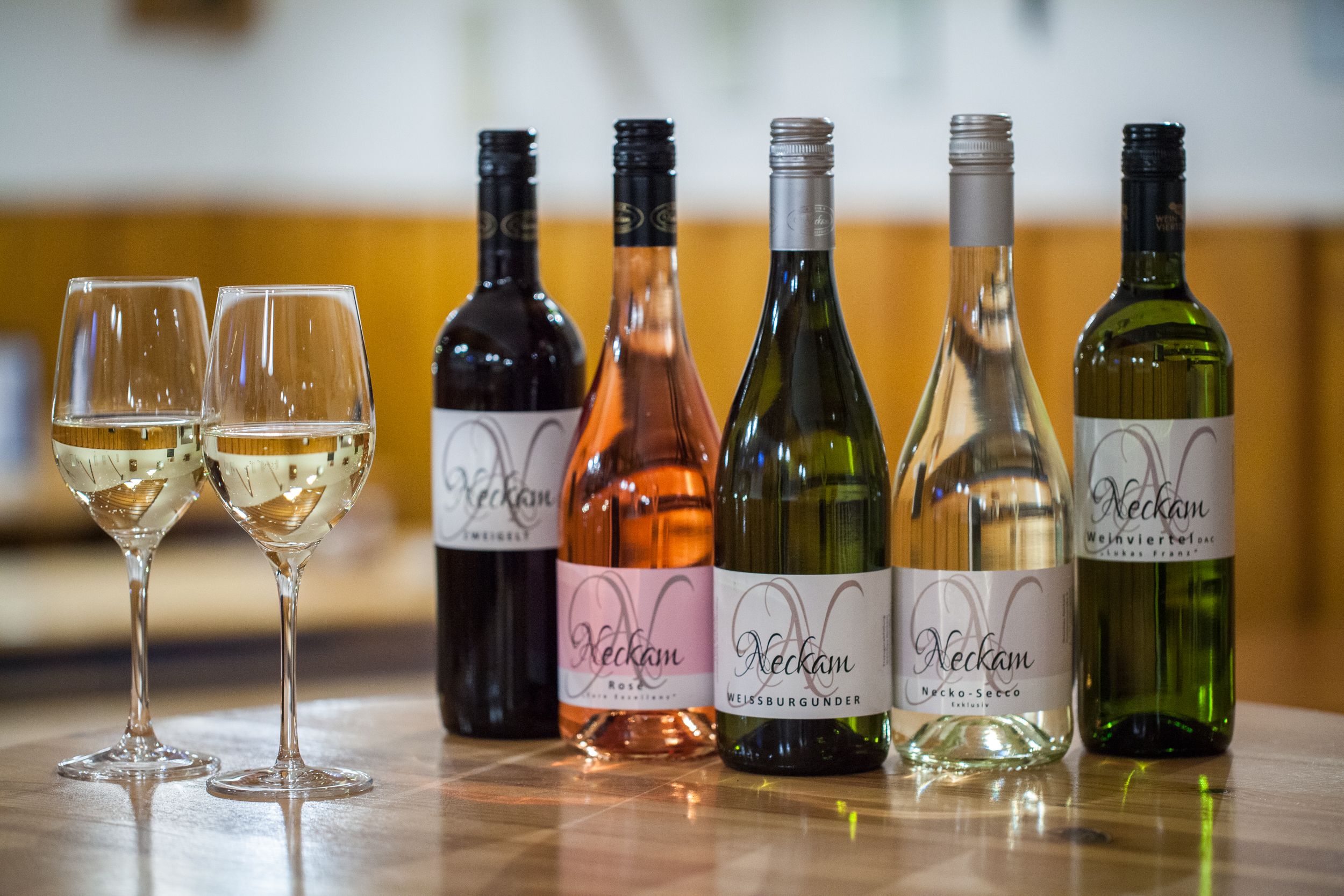 Pět lahví vína a dvě plné sklenice na dřevěném stole.