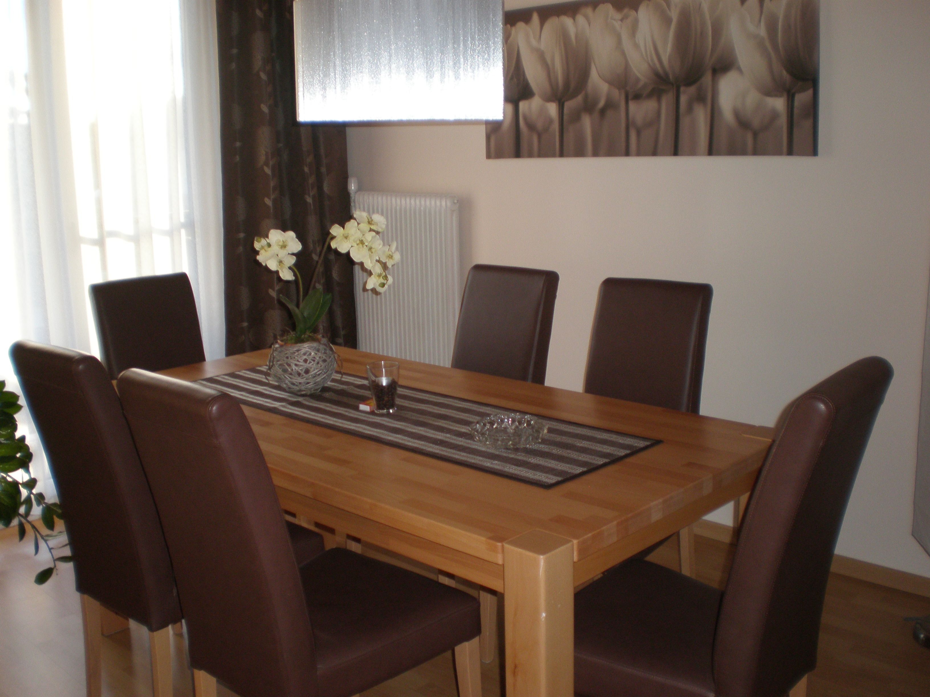 Jídelna s dřevěným stolem, šesti hnědými židlemi a orchidejí jako dekorací.