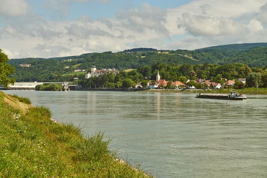 Říční krajina s vesnicí a kopci v pozadí.