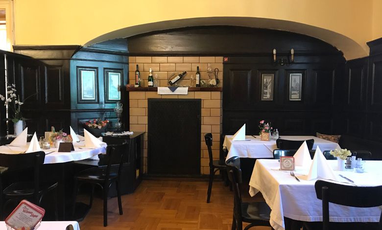 Pohled do interiéru tradiční restaurace s tmavým dřevěným obložením a prostřenými stoly.