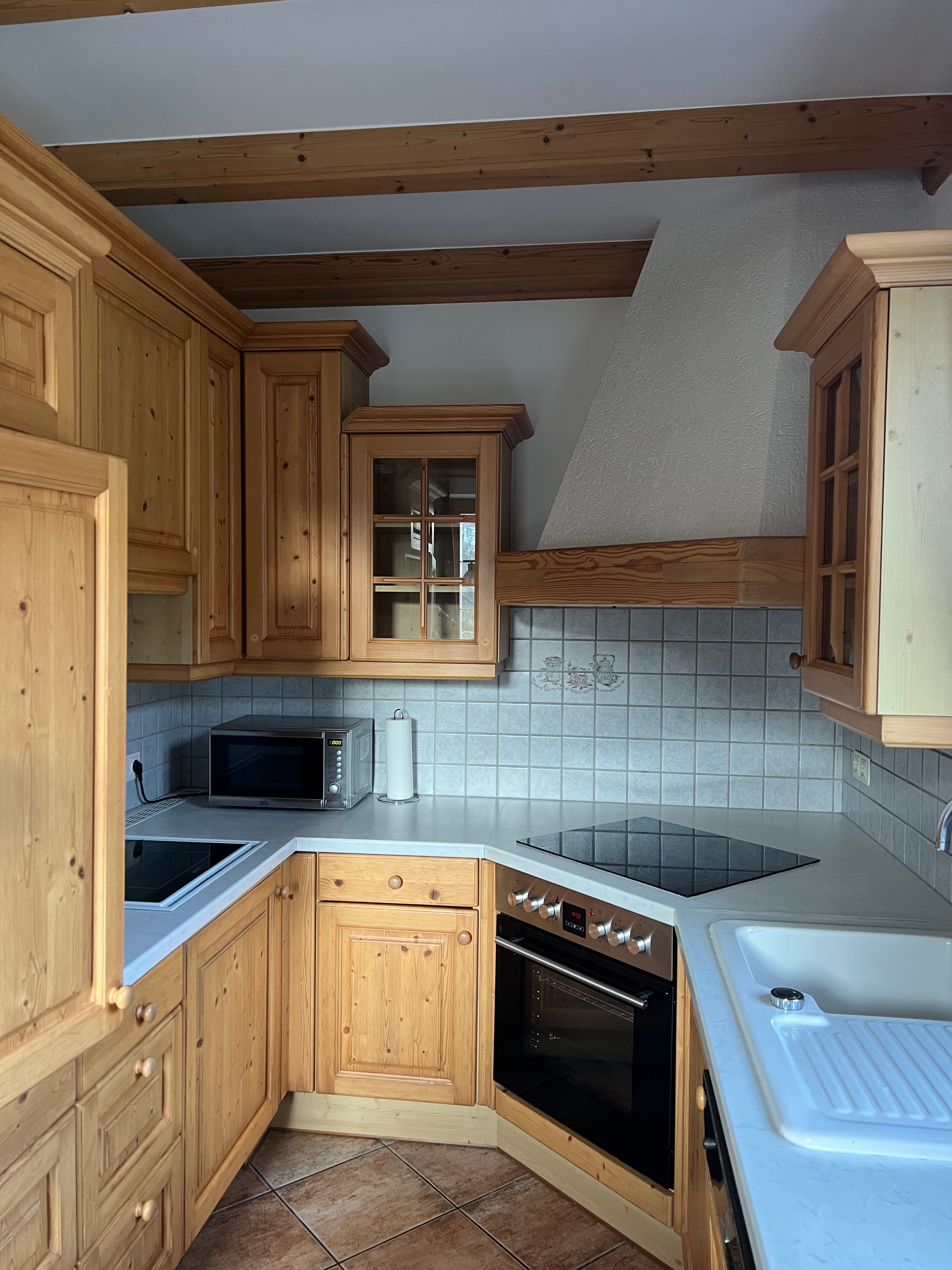 Rustikální kuchyně s dřevěnými skříňkami, elektrickým sporákem, mikrovlnnou troubou a dřezem. Stěny jsou obložené dlaždicemi.