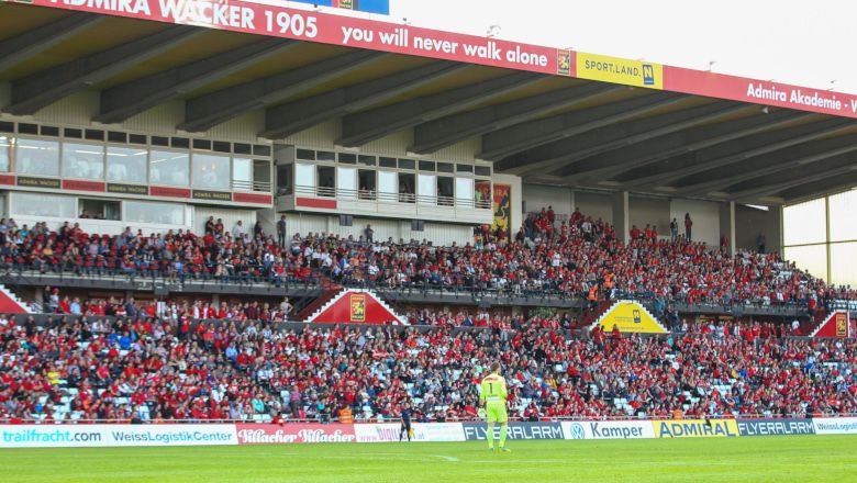 Fotbalový stadion s plnými tribunami a hráčem na hřišti.
