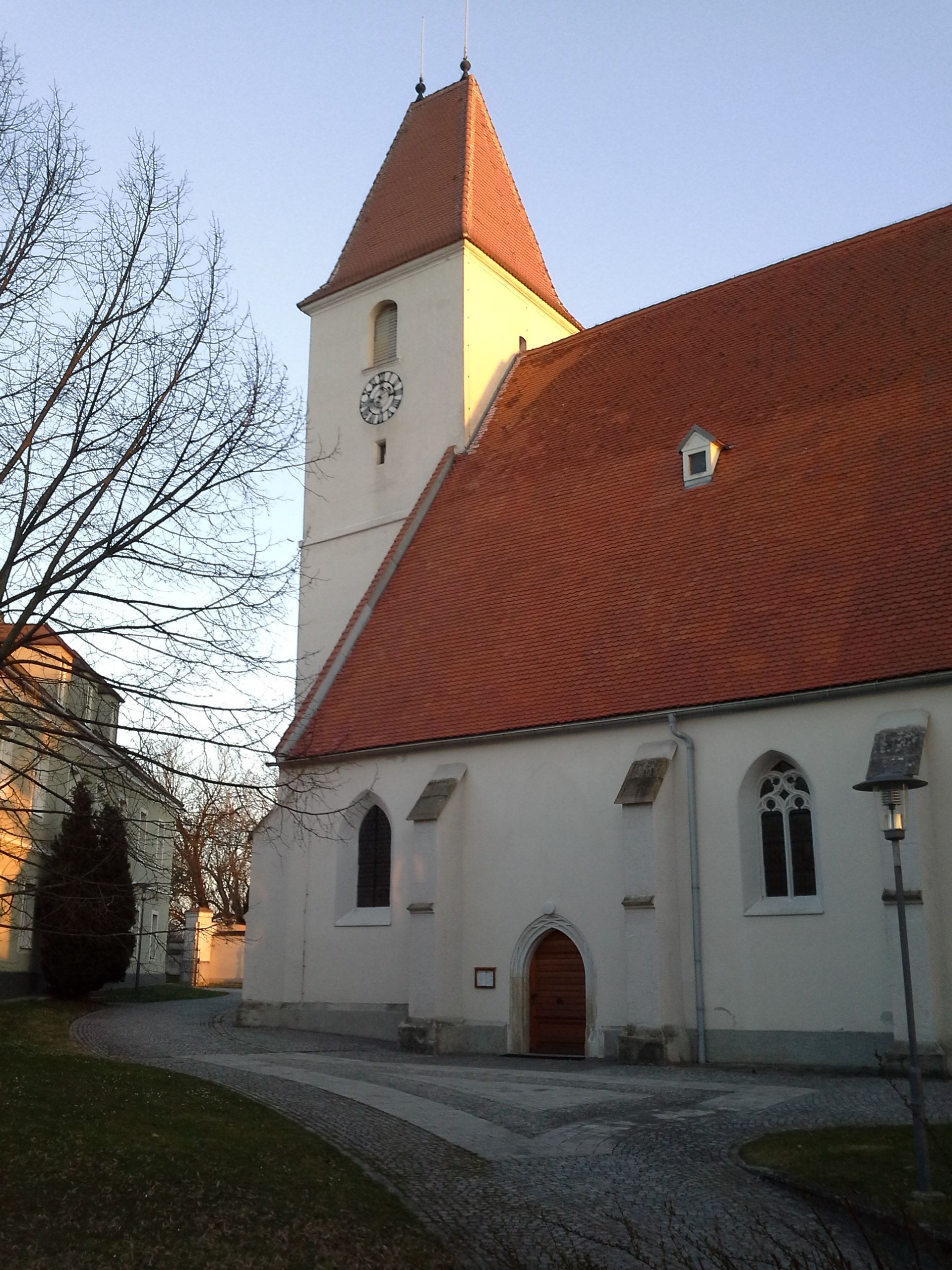 Kostel s červenou střechou a hodinovou věží v Kapellnu při západu slunce.