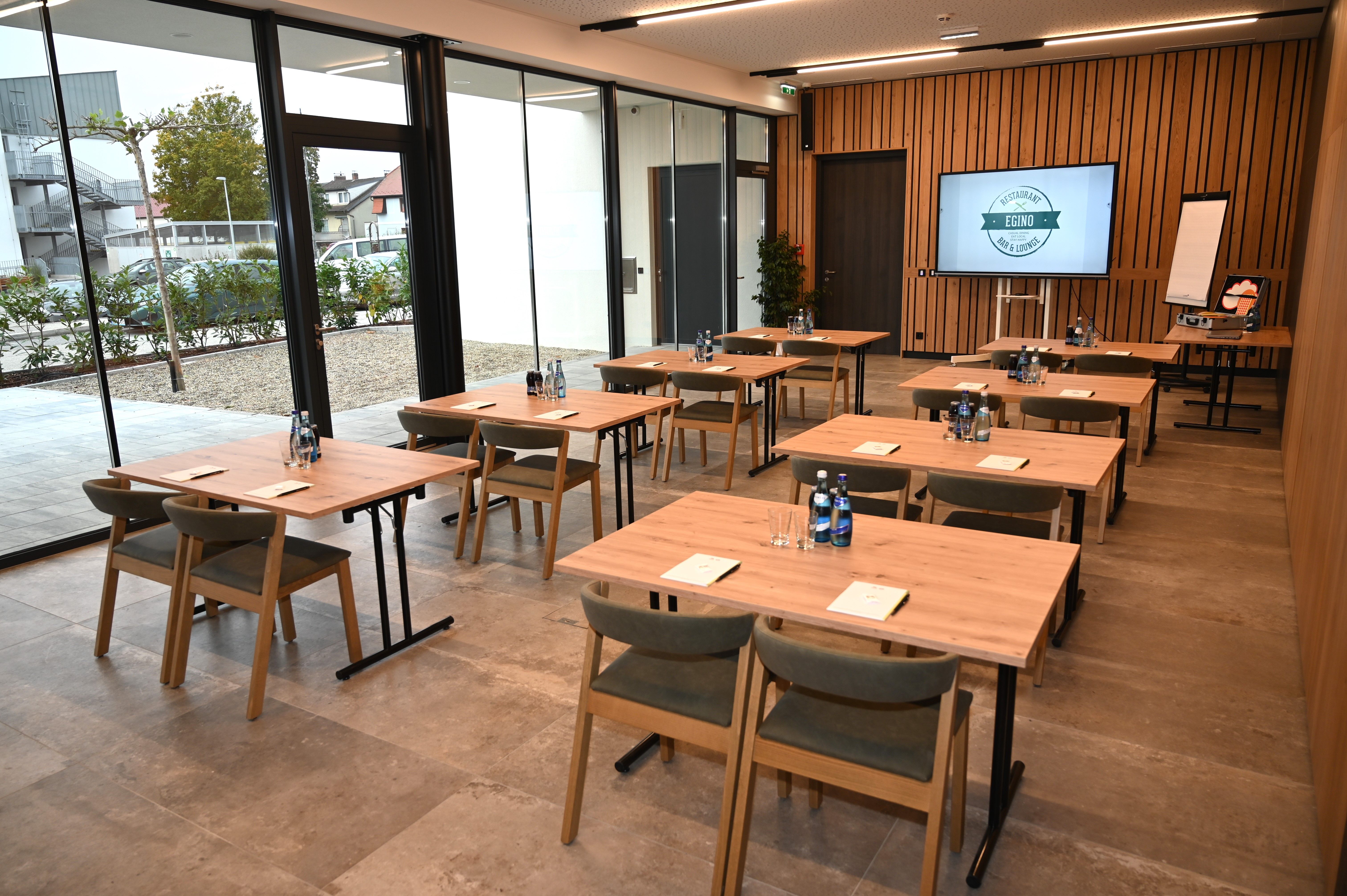 Moderní seminární místnost s dřevěnými stoly, židlemi a prezentační technikou.