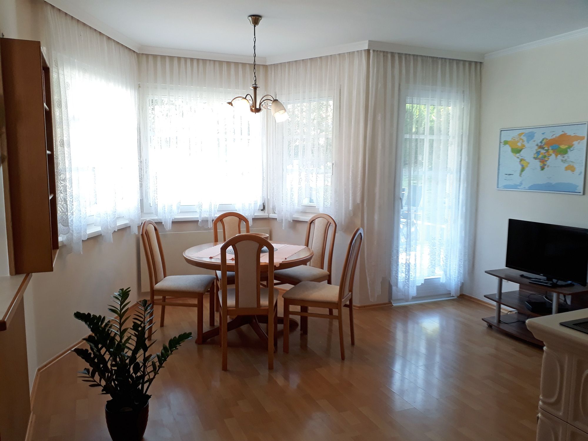 Světlá kuchyně s jídelním stolem, židlemi, TV a mapou světa na stěně.