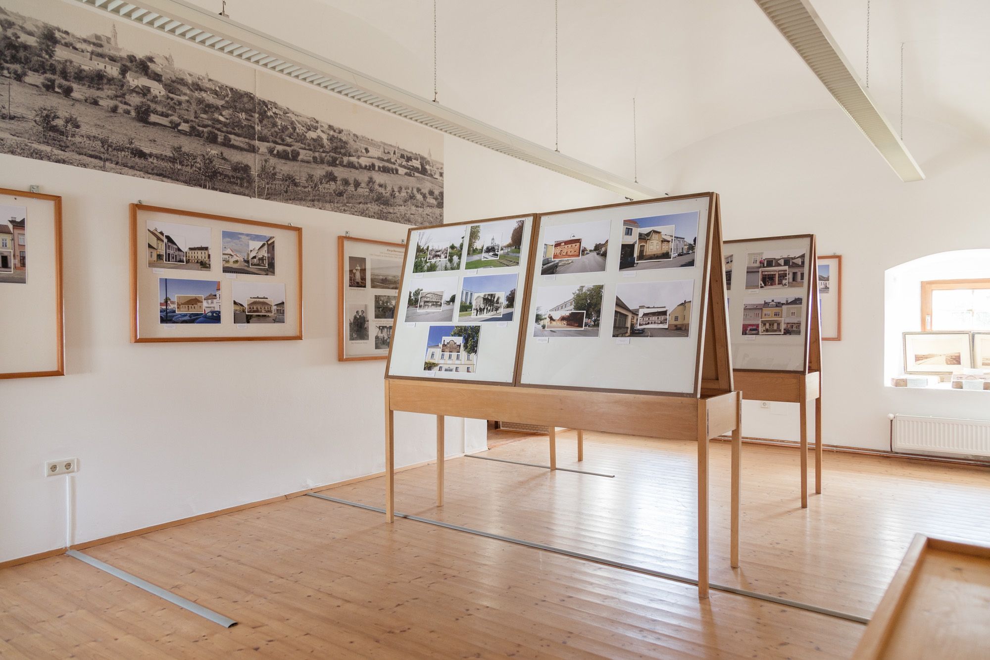 Pohled do interiéru muzejní místnosti s fotografickými panely a historickými obrazy na stěnách.