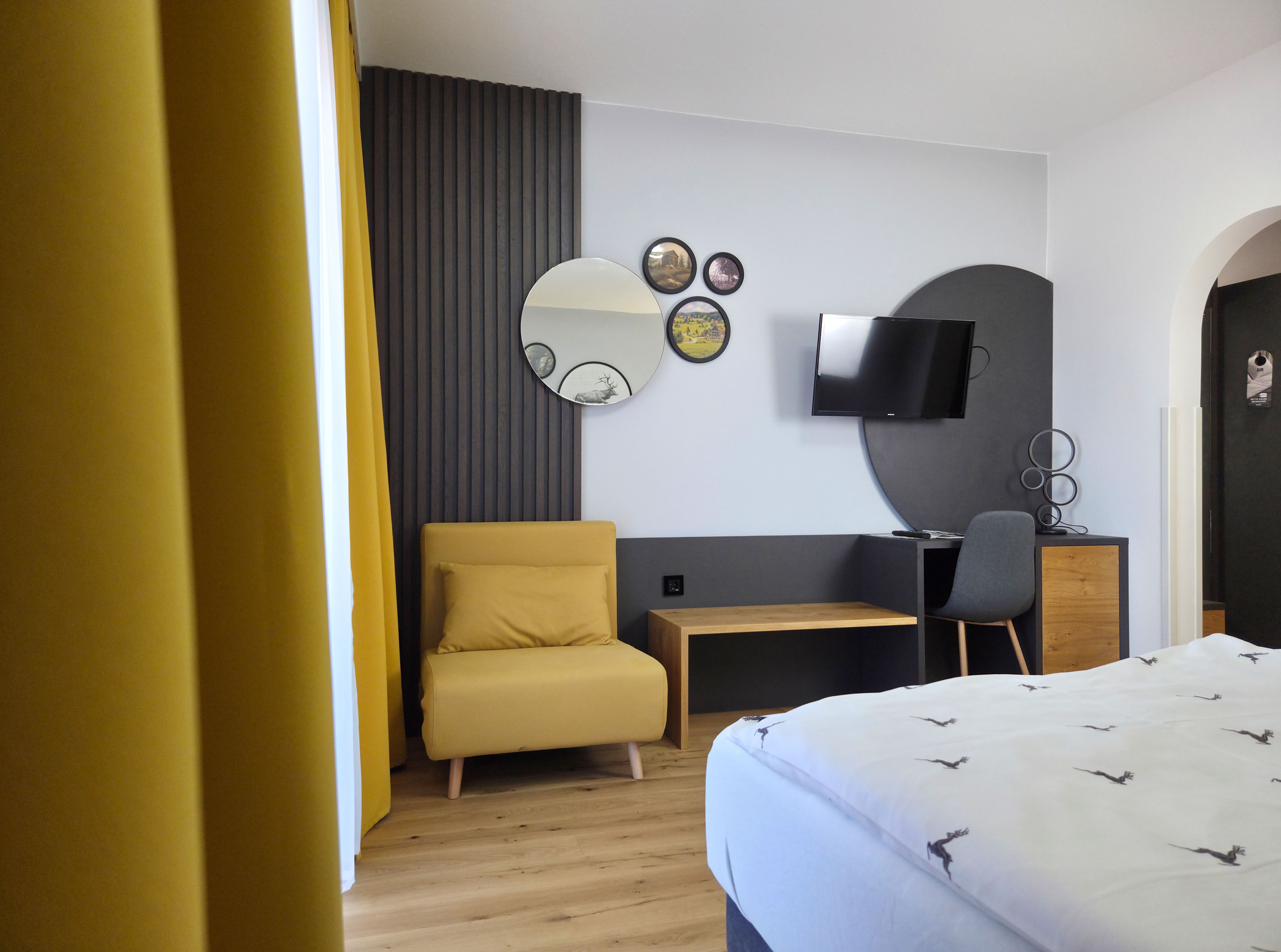Moderně zařízený pokoj se žlutým křeslem, zrcadly na stěnách, televizí a psacím stolem s židlí.