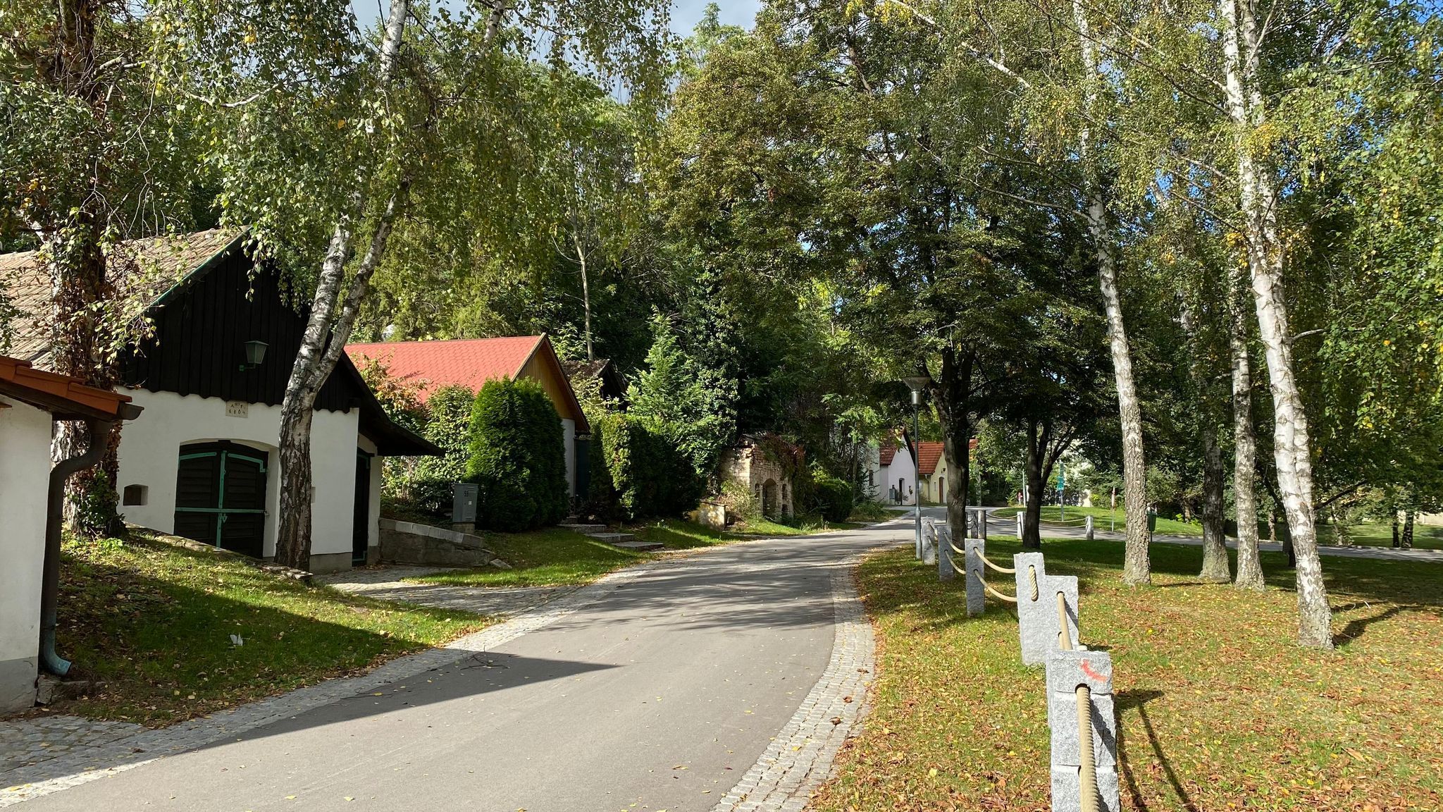 Malebná ulice (řada sklepů) s malými domky a stromy ve venkovském prostředí.