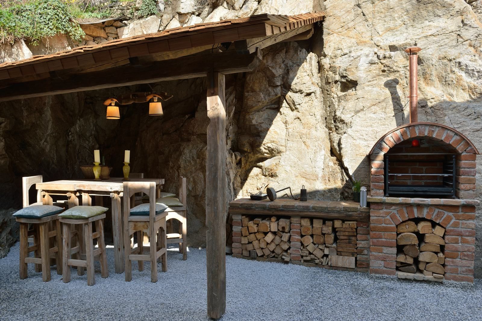 Rustikální venkovní prostor s dřevěným stolem, židlemi a zděnou pecí.