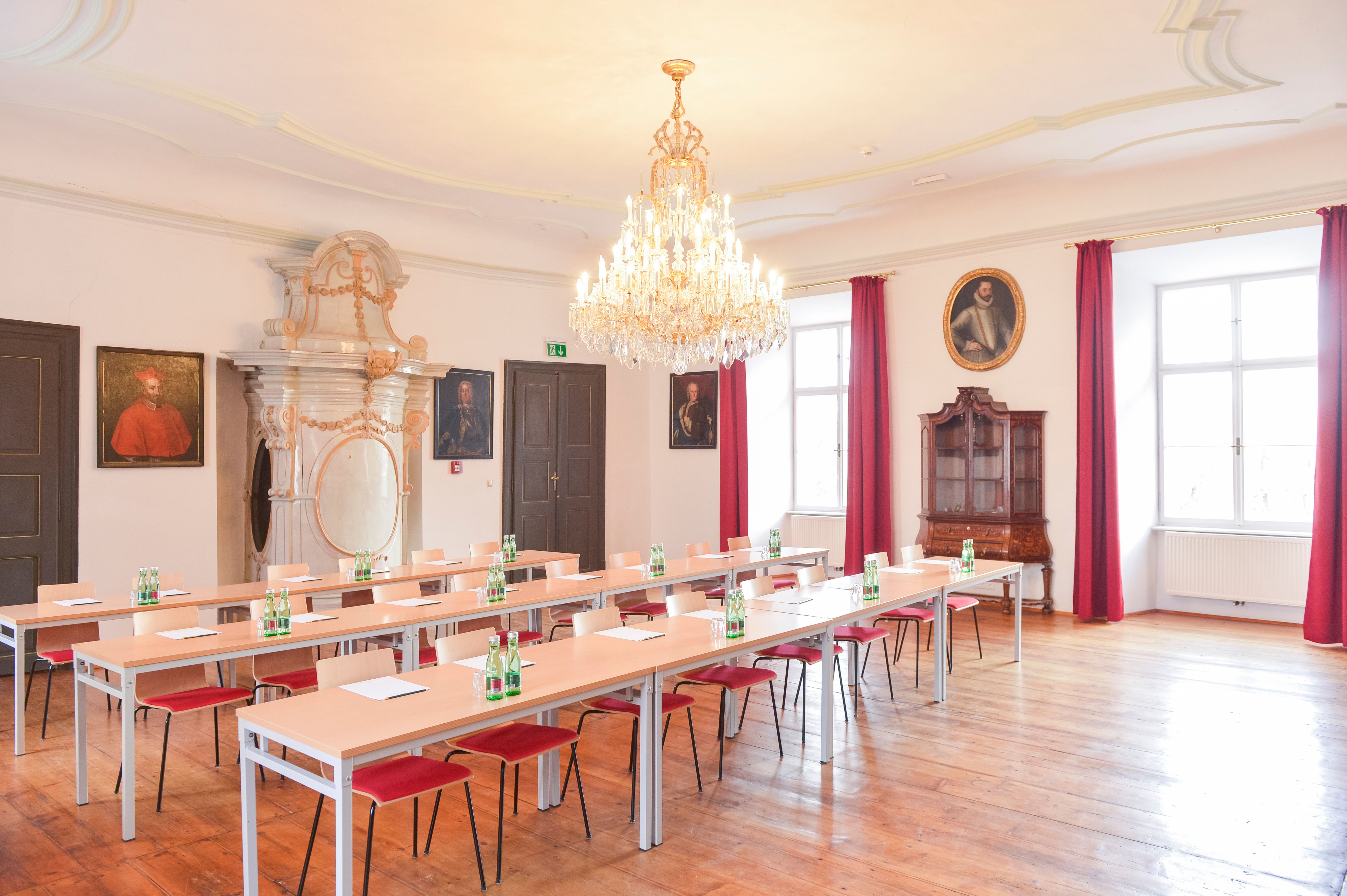 Elegantní seminární místnost s lustrem, dřevěnou podlahou a portréty na stěnách.