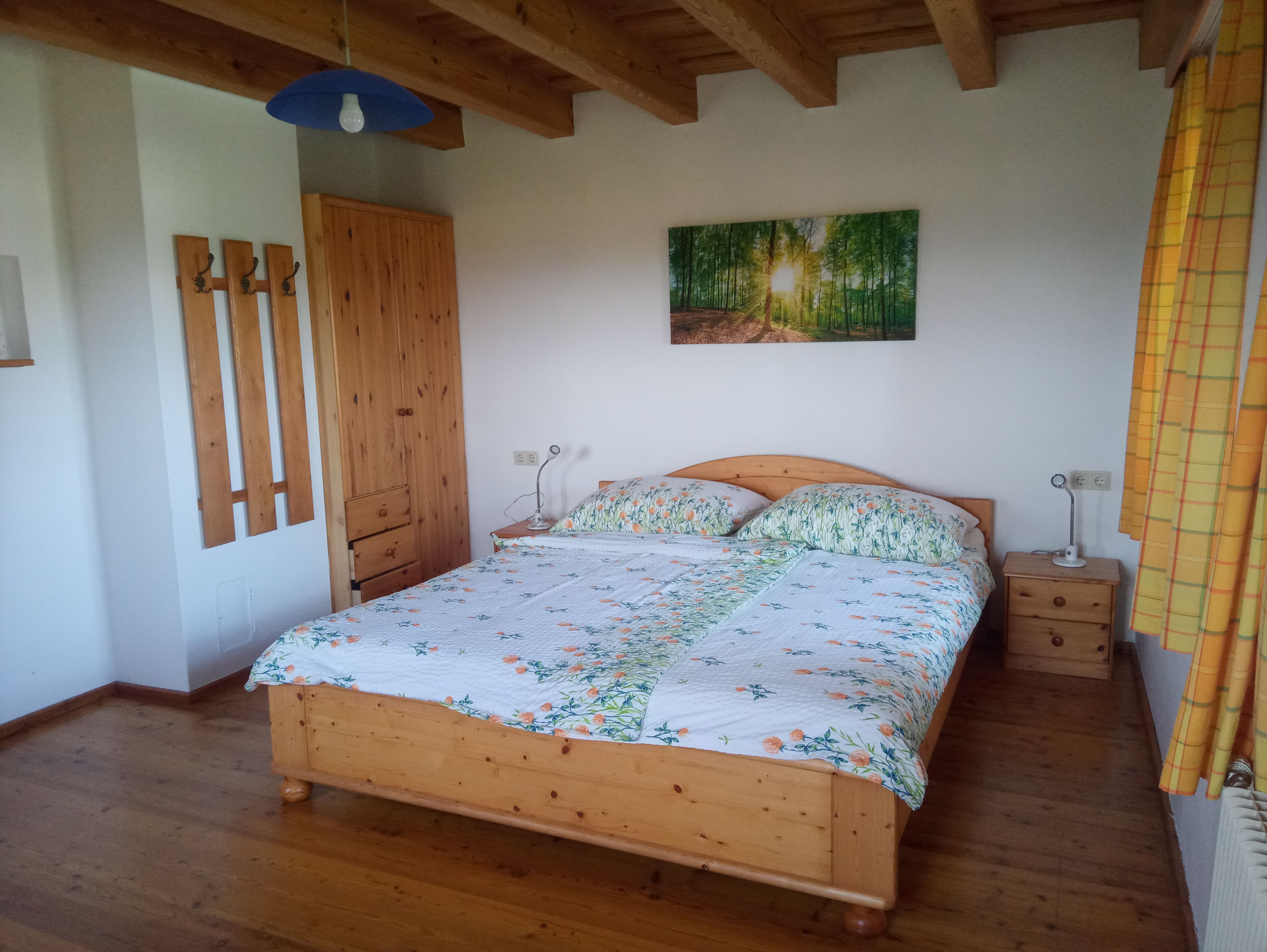 Ložnice s dřevěnou postelí, nočními stolky, šatní skříní a nástěnnou malbou lesa.