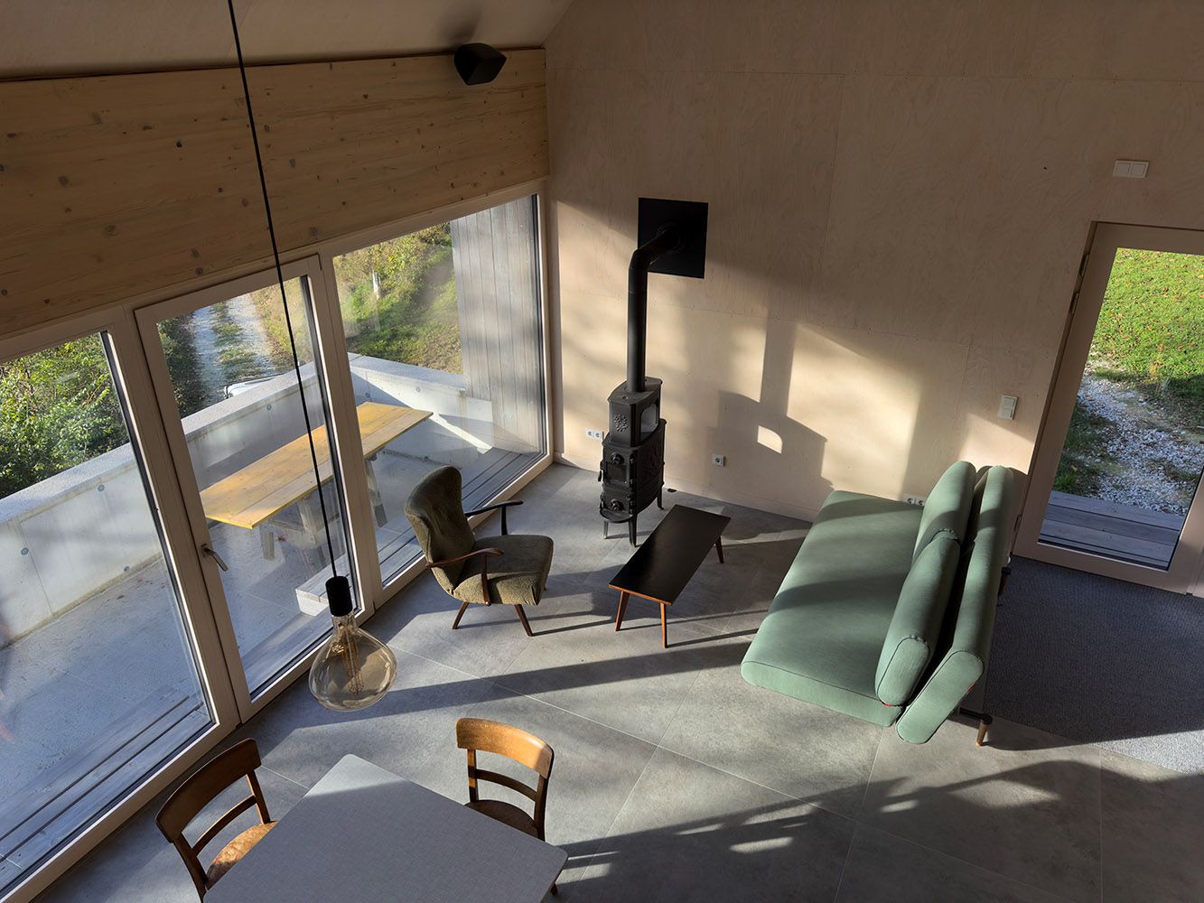 Moderní obývací a jídelní prostor s velkými okny, pohovkou, křeslem a krbem.