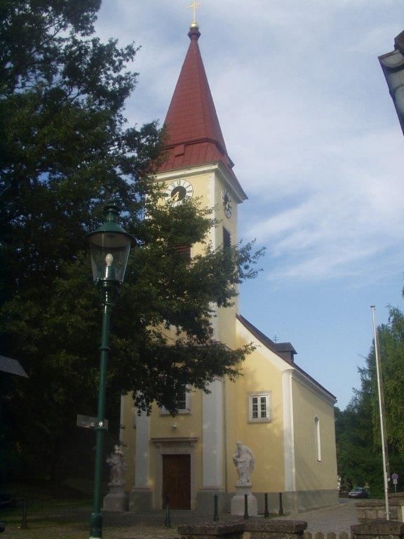 Vnější pohled na farní kostel v Sulzu s věží a hodinami.