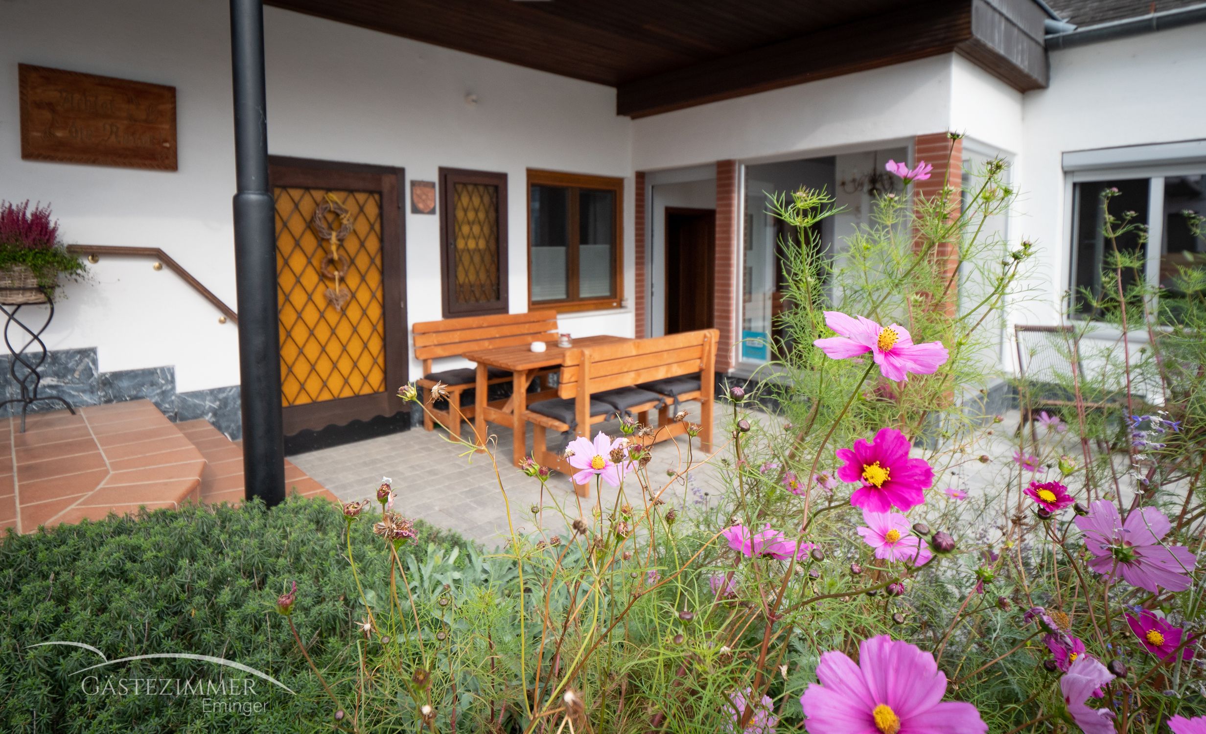 Terasa s dřevěným nábytkem a rozkvetlými květinami v popředí.