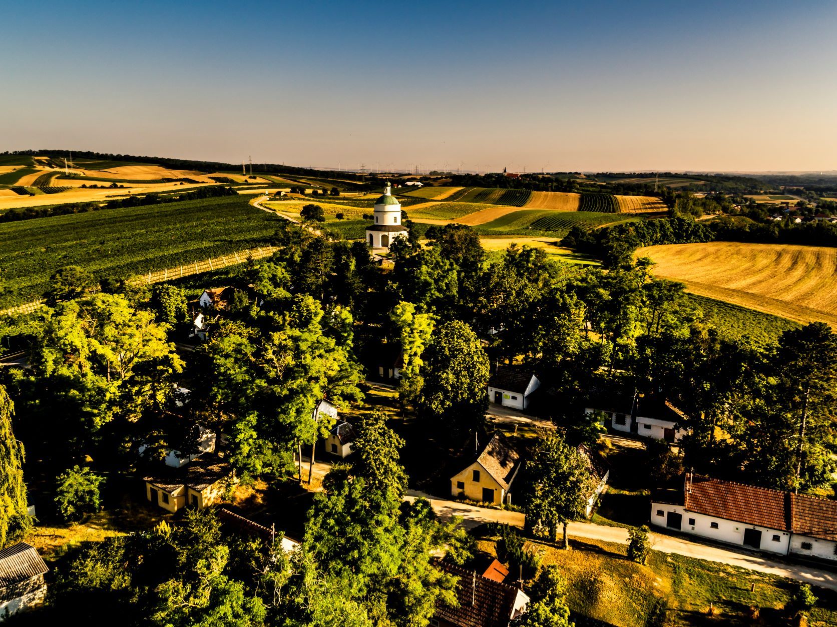 Krajina s poli, stromy a kostelíkem uprostřed.