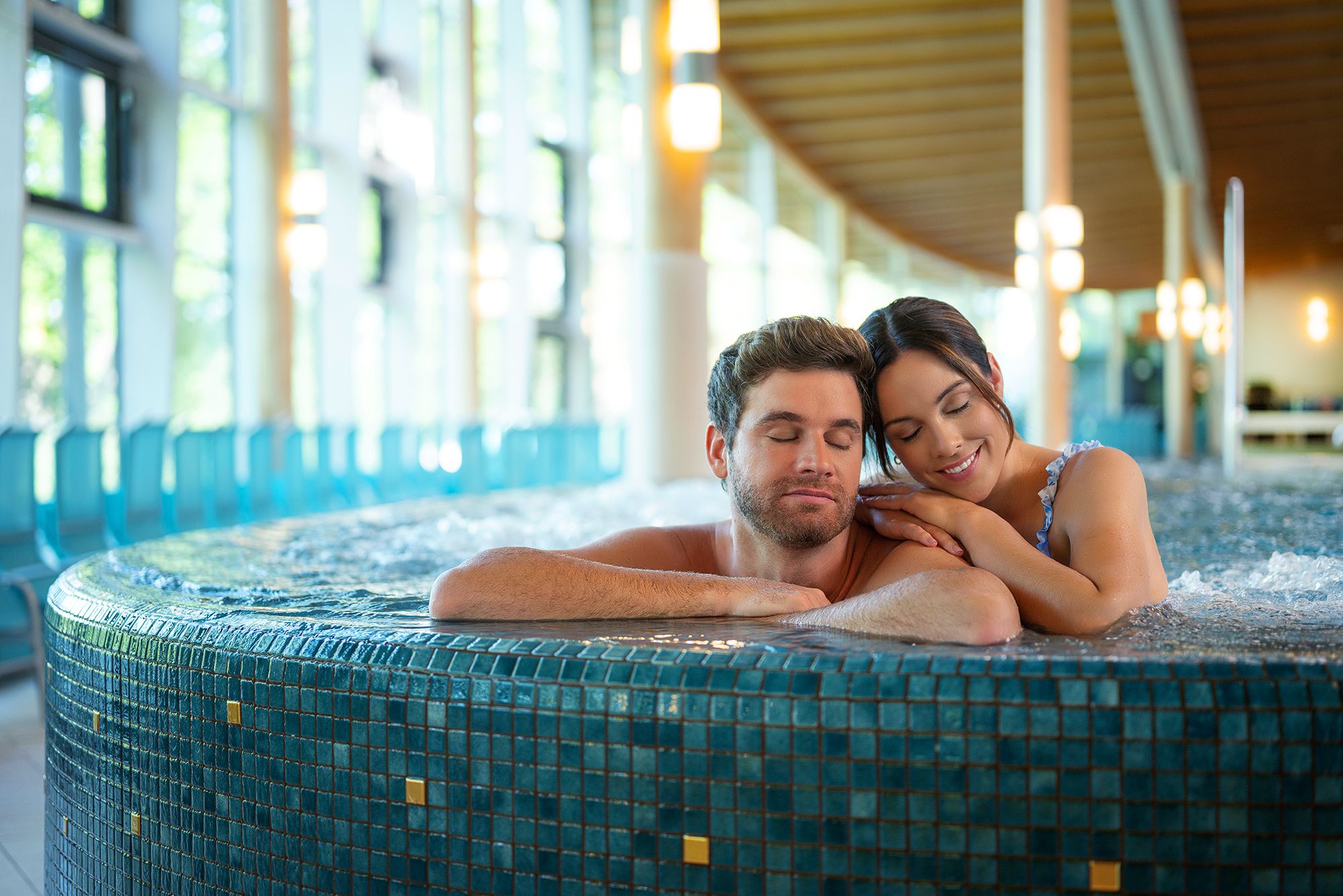 Pár relaxuje ve vířivce v moderním wellness centru s velkými okny.