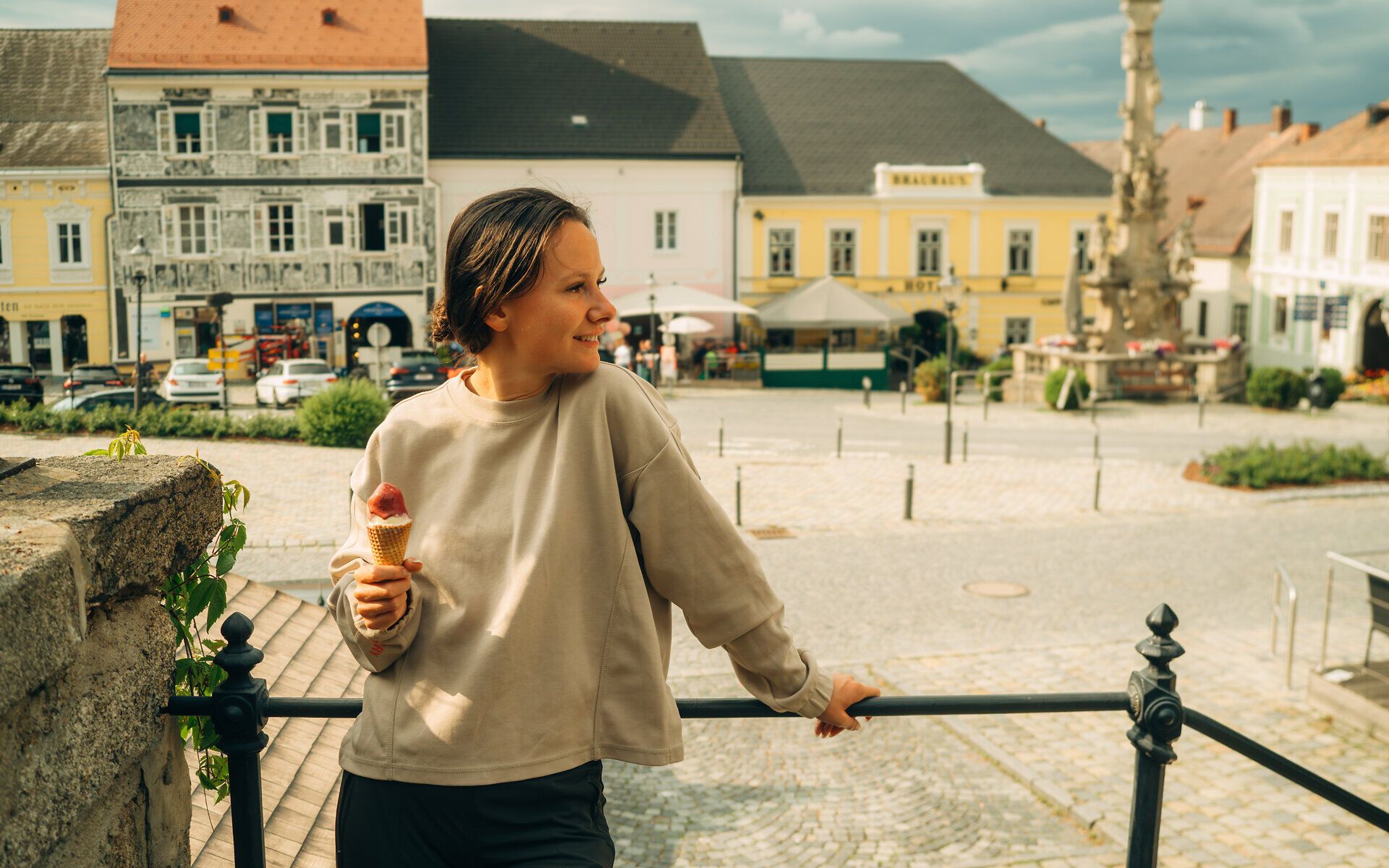 Žena stojí před zábradlím, dívá se na hlavní náměstí ve Weitře a v ruce drží zmrzlinu.