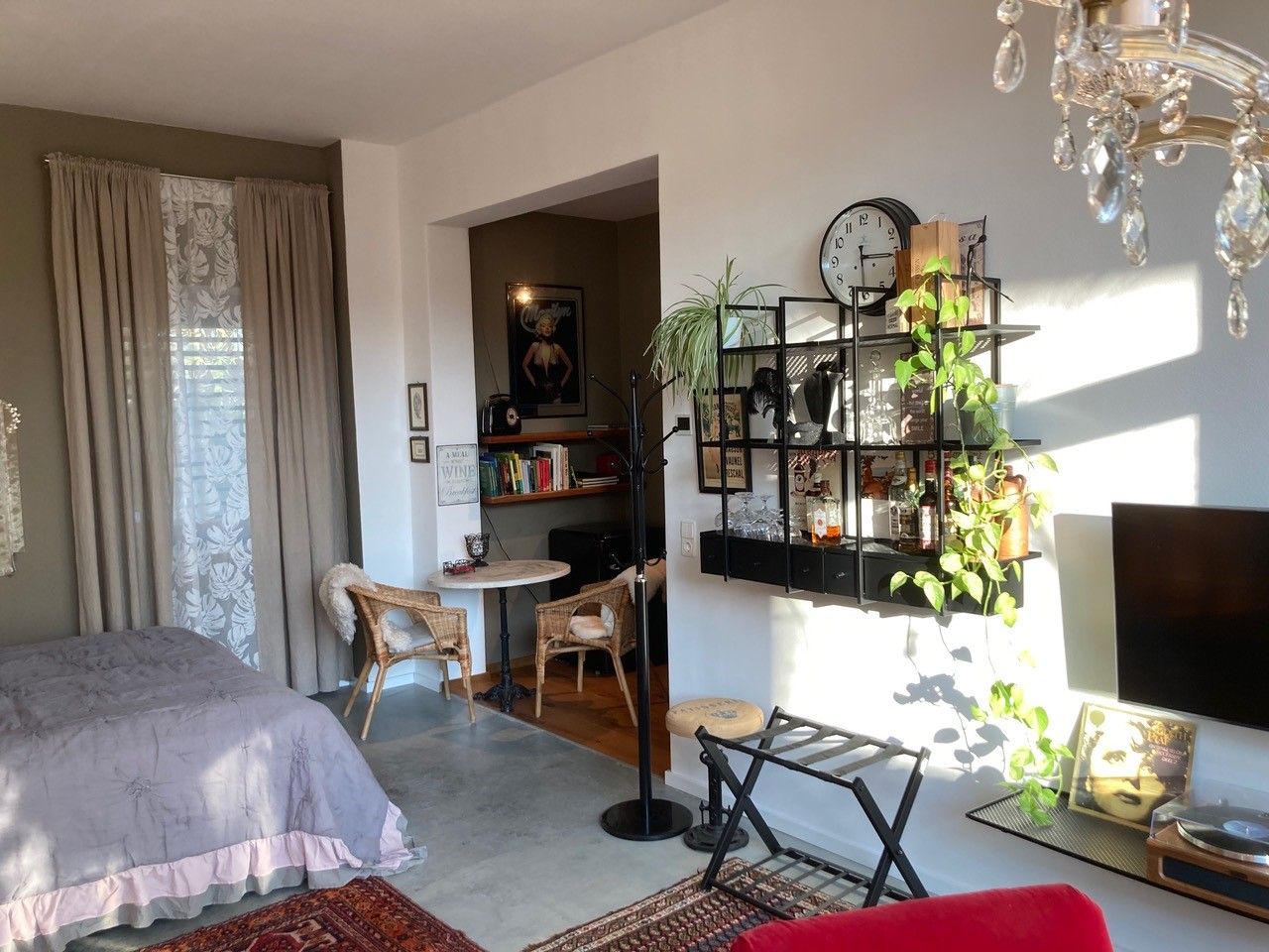 Útulný obývací pokoj s postelí, poličkou, rostlinami a nástěnnou dekorací.