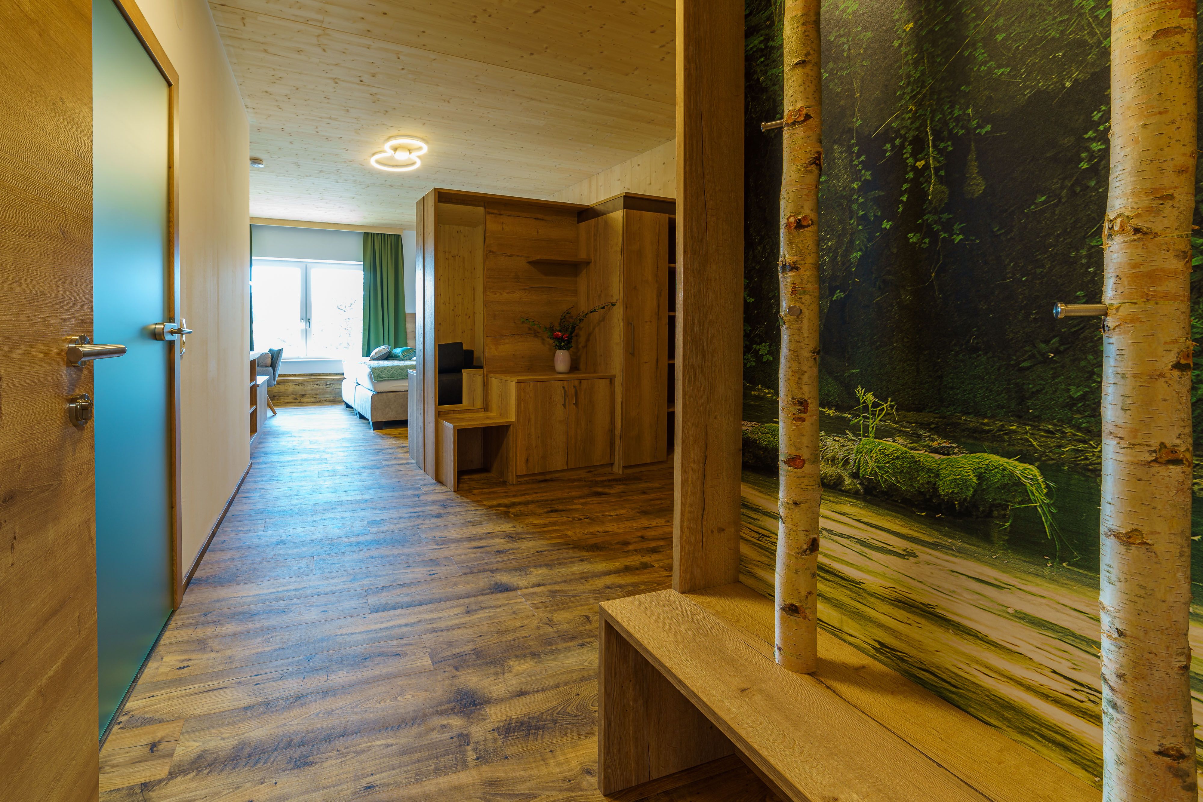 Pohled do interiéru moderního bytu s dřevěnou podlahou, dřevěným nábytkem a velkým oknem.