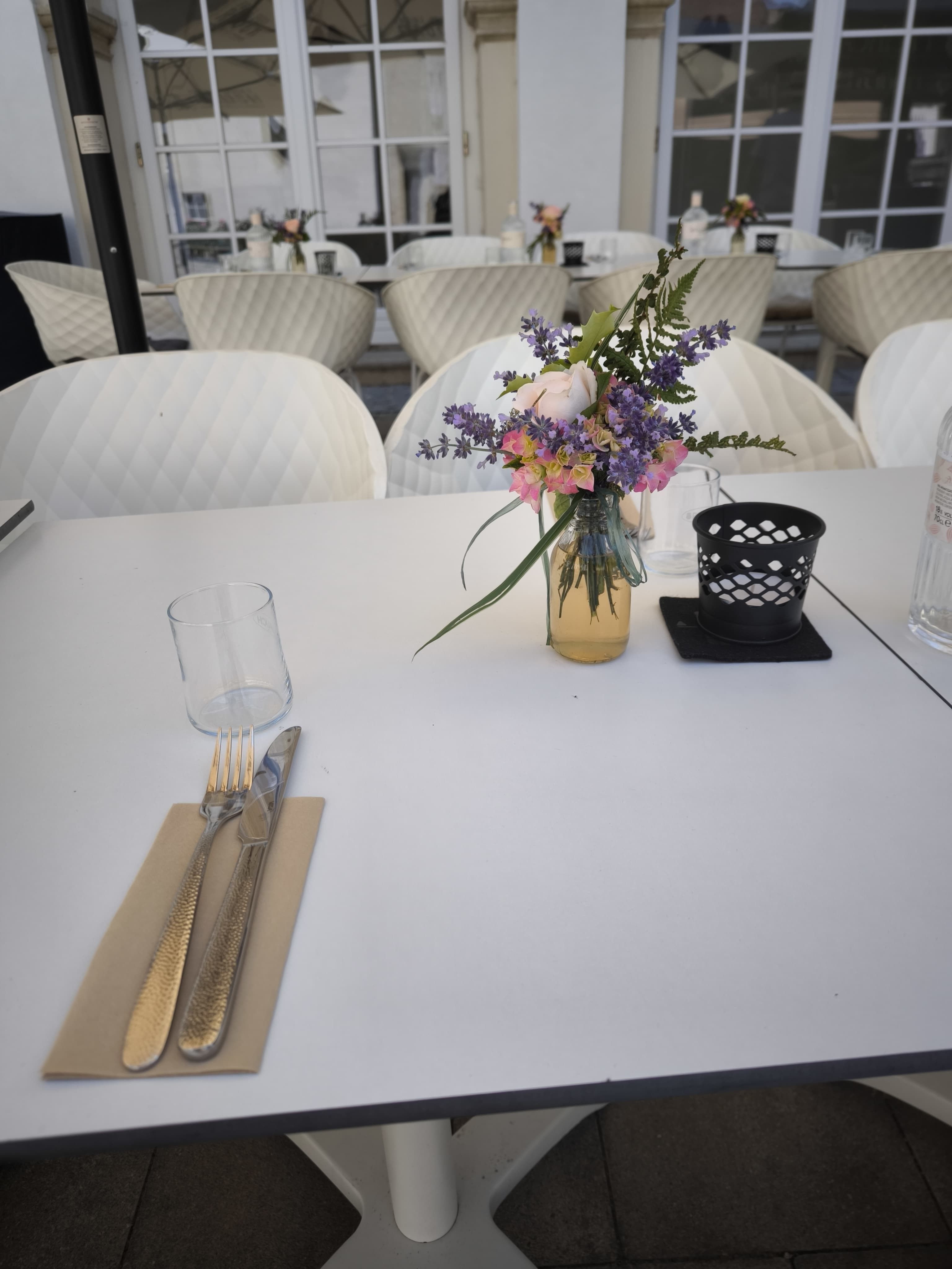 Prostření stolu na terase s kyticí květin a příbory.