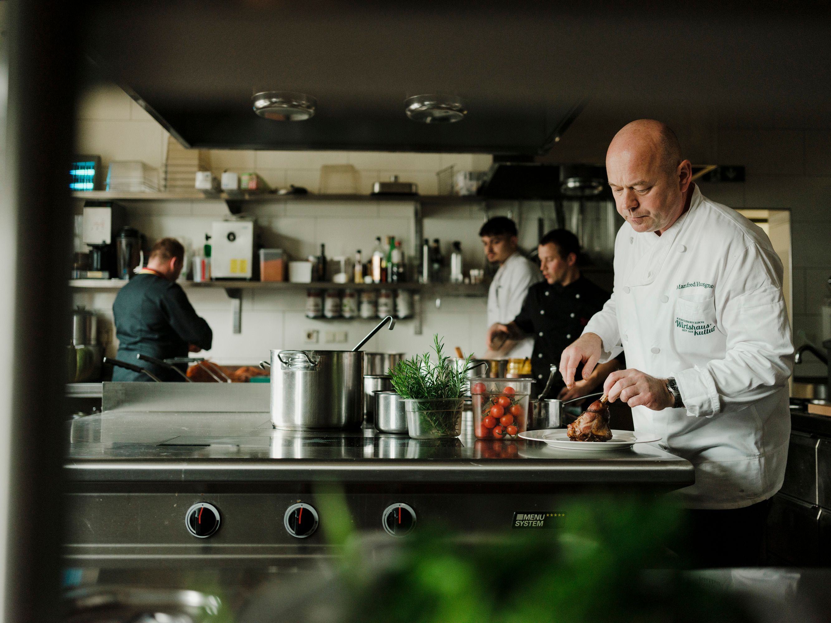 Kuchaři pracují v profesionální kuchyni, jeden krájí maso.