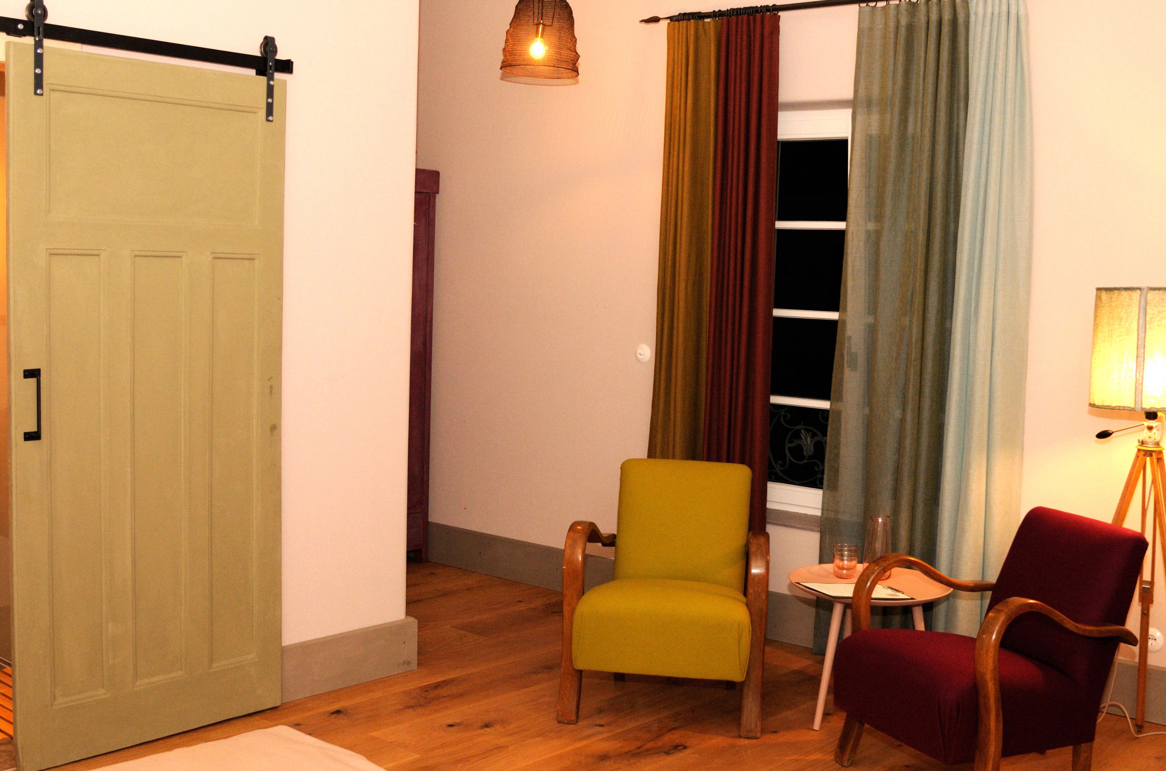 Útulný pokoj se dvěma křesly, malým stolkem a lampou. K vidění jsou také posuvné dveře a barevné závěsy.