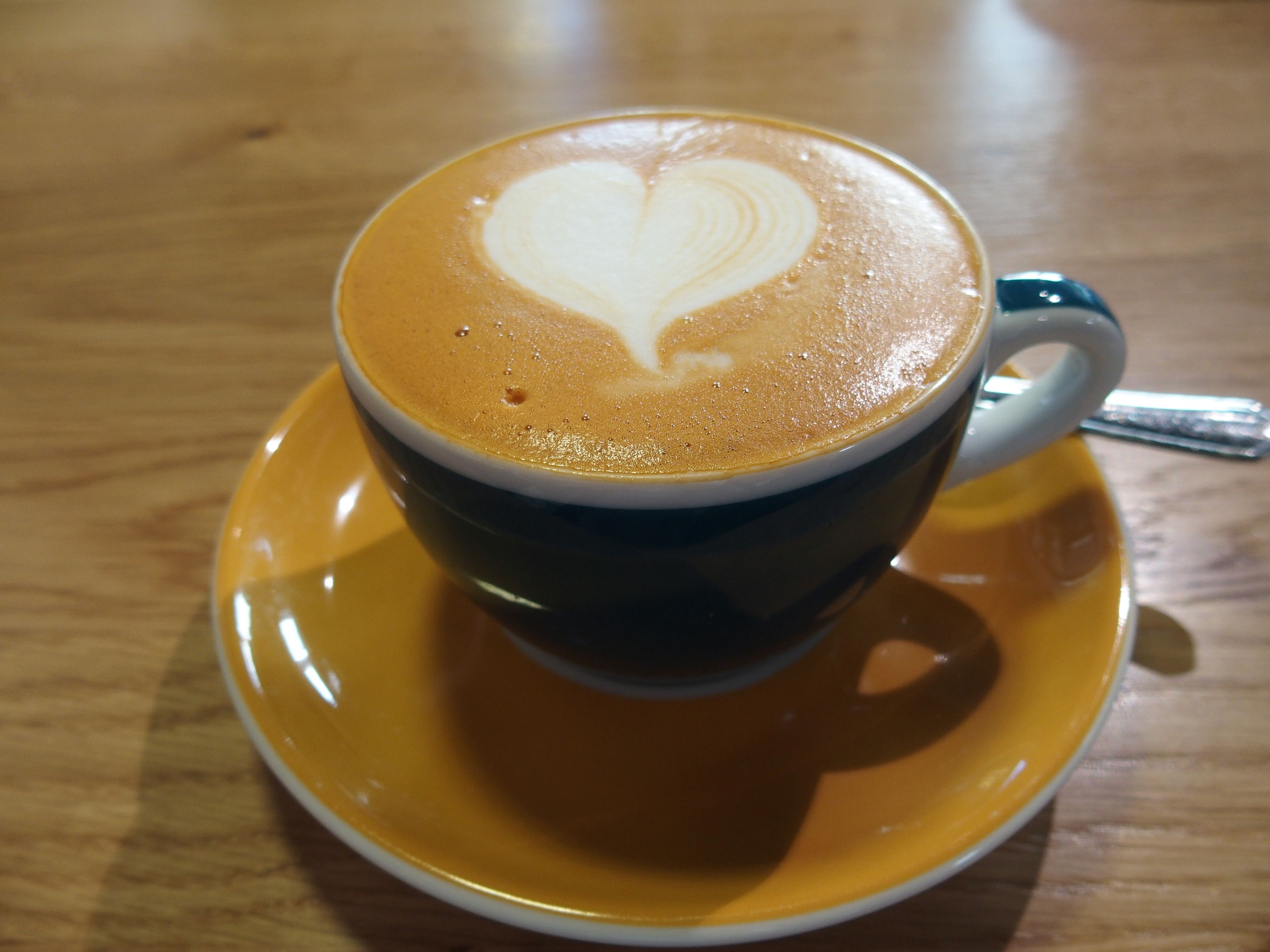 Šálek cappuccina s latté ve tvaru srdce na dřevěném stole.