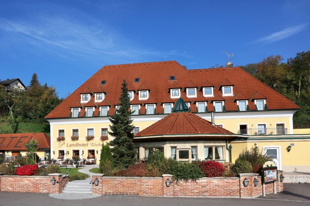 Pohled zvenčí na žlutý venkovský hotel s červenou střechou a zahradou.