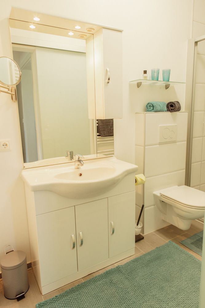 Moderní koupelna s umyvadlem, zrcadlem, toaletou a poličkami.