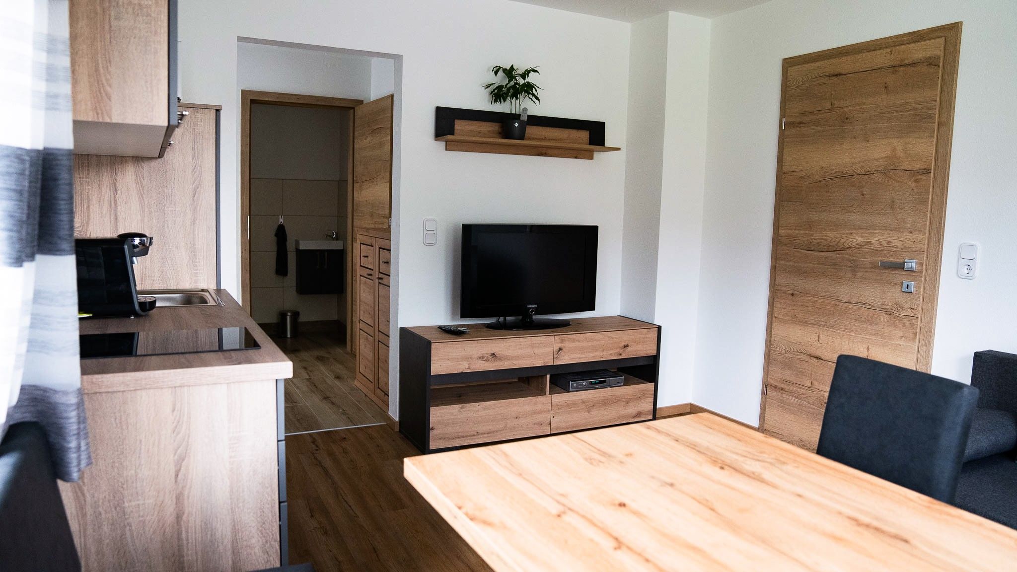 Moderní obývací pokoj s dřevěným nábytkem, TV a kuchyní.