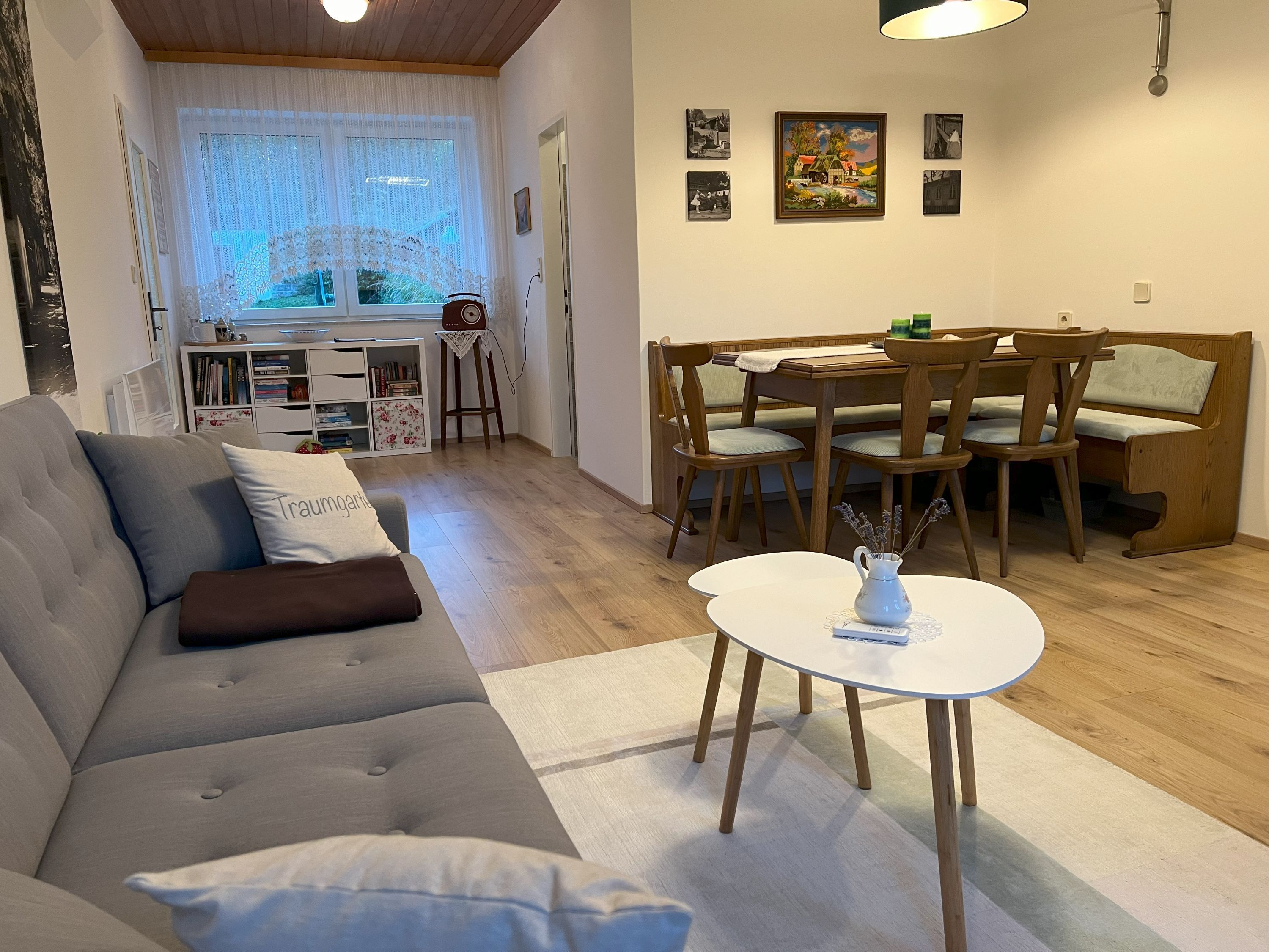 Útulný obývací pokoj s šedou pohovkou, jídelním stolem a židlemi, knihovnou a oknem se závěsy.