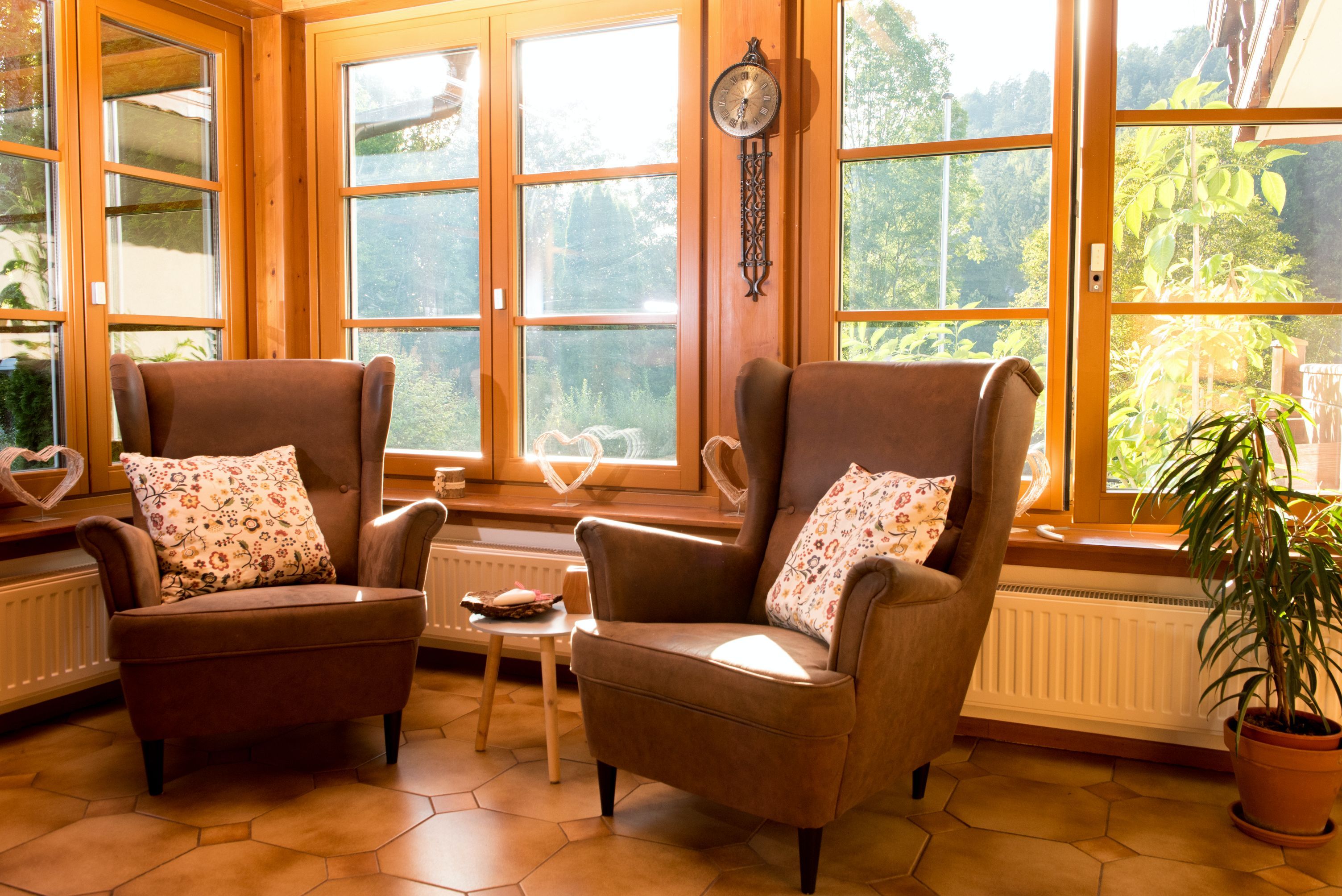 Dvě hnědá křesla se vzorovanými polštáři před velkými okny ve slunné místnosti.