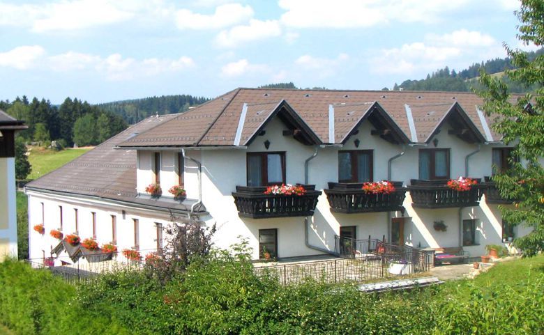 Velká bílá budova s hnědými střechami a balkony s květinami.