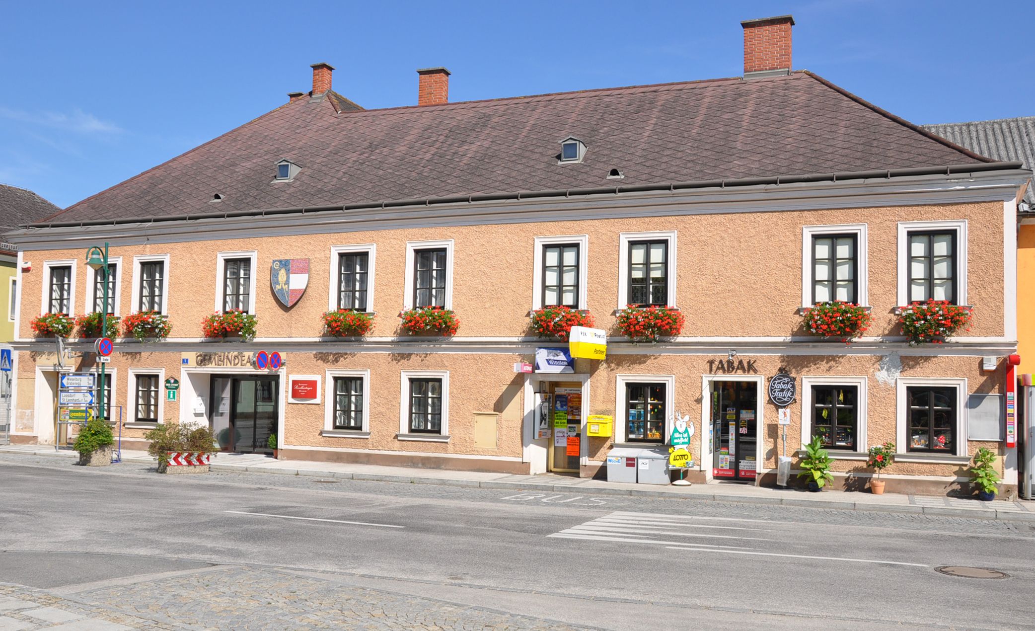 Dvoupatrová budova s květinami v oknech a obchody v přízemí v Ruprechtshofenu.