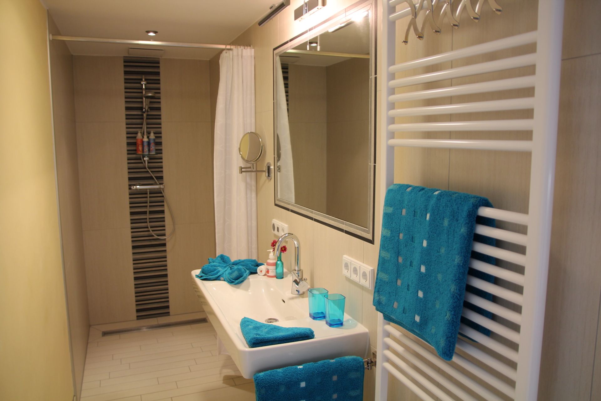 Moderní koupelna se sprchou, umyvadlem a modrými ručníky.