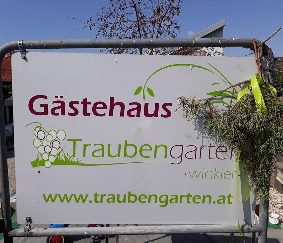Tabulka s nápisem "Gästehaus Traubengarten Winkler" a internetovou adresou, zdobená větvemi.