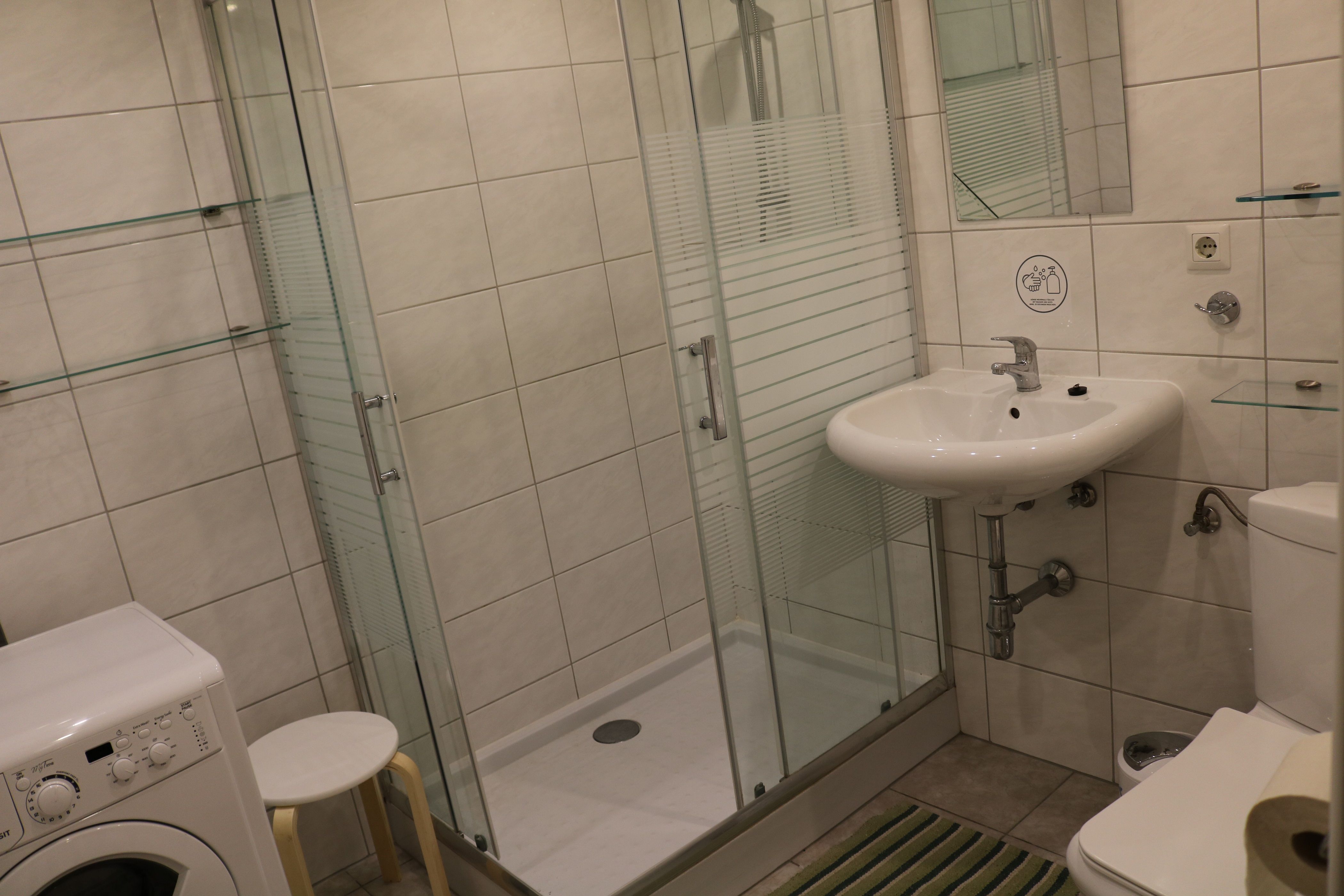 Moderní koupelna se sprchovým koutem, umyvadlem, toaletou a pračkou.