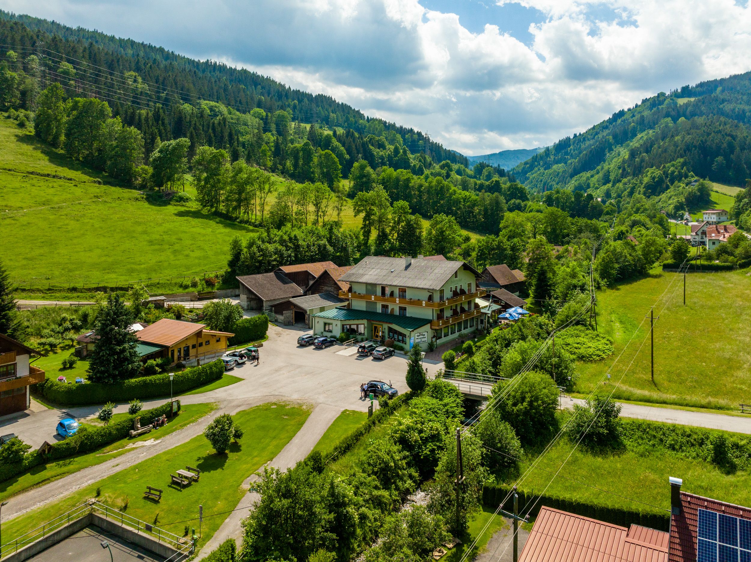 Venkovská krajina s velkou budovou obklopenou zelenými kopci a stromy.