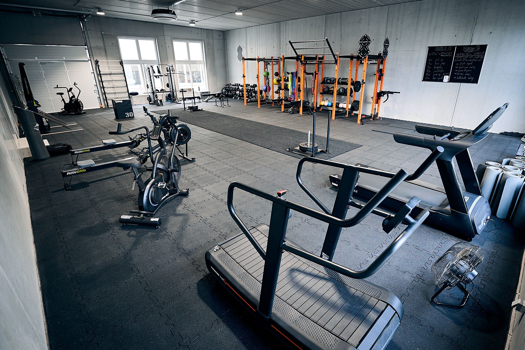 Pohled do interiéru fitness studia s různým tréninkovým vybavením, jako jsou běžecké pásy, jízdní kola a činky.