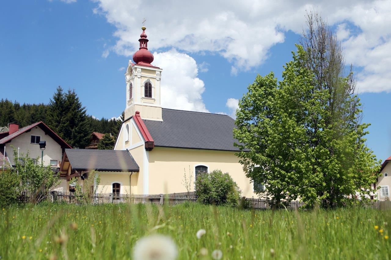 Kostel v Mitterbachu s červenou věží a zeleným stromem v popředí.