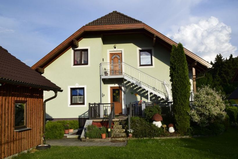 Dvoupodlažní dům se zeleným nátěrem a venkovním schodištěm v zahradě.