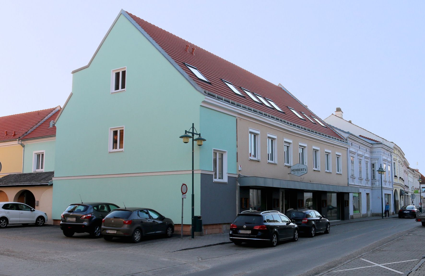 Scéna na ulici Traismauer s několikapatrovou budovou a zaparkovanými auty.
