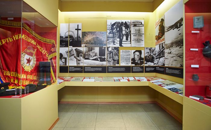 Výstavní místnost s historickými fotografiemi, dokumenty a červenou vlajkou.