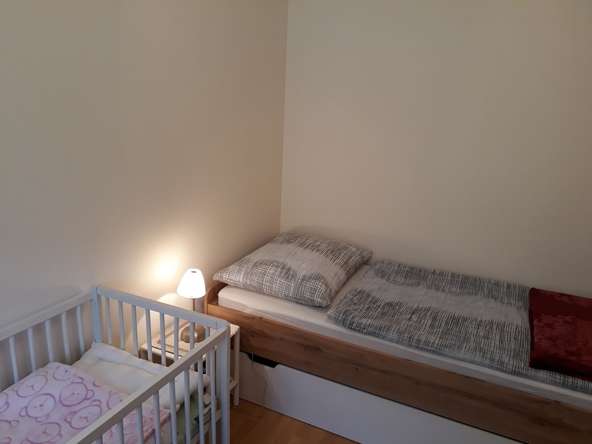 Jednolůžkový pokoj s jednou postelí, dětskou postýlkou a noční lampičkou.