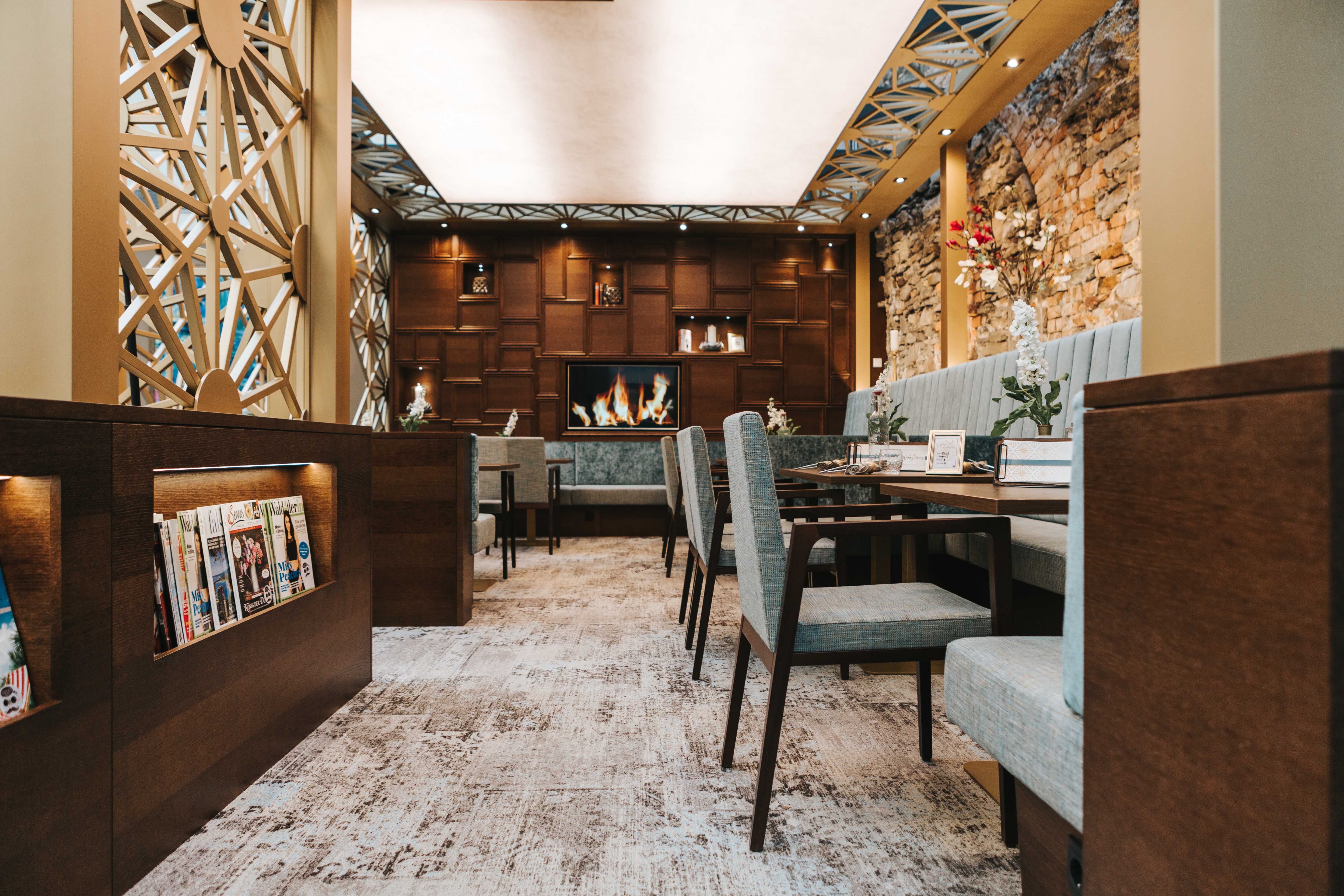 Pohled do interiéru stylové kavárny s útulným posezením, krbem a stojanem na časopisy.