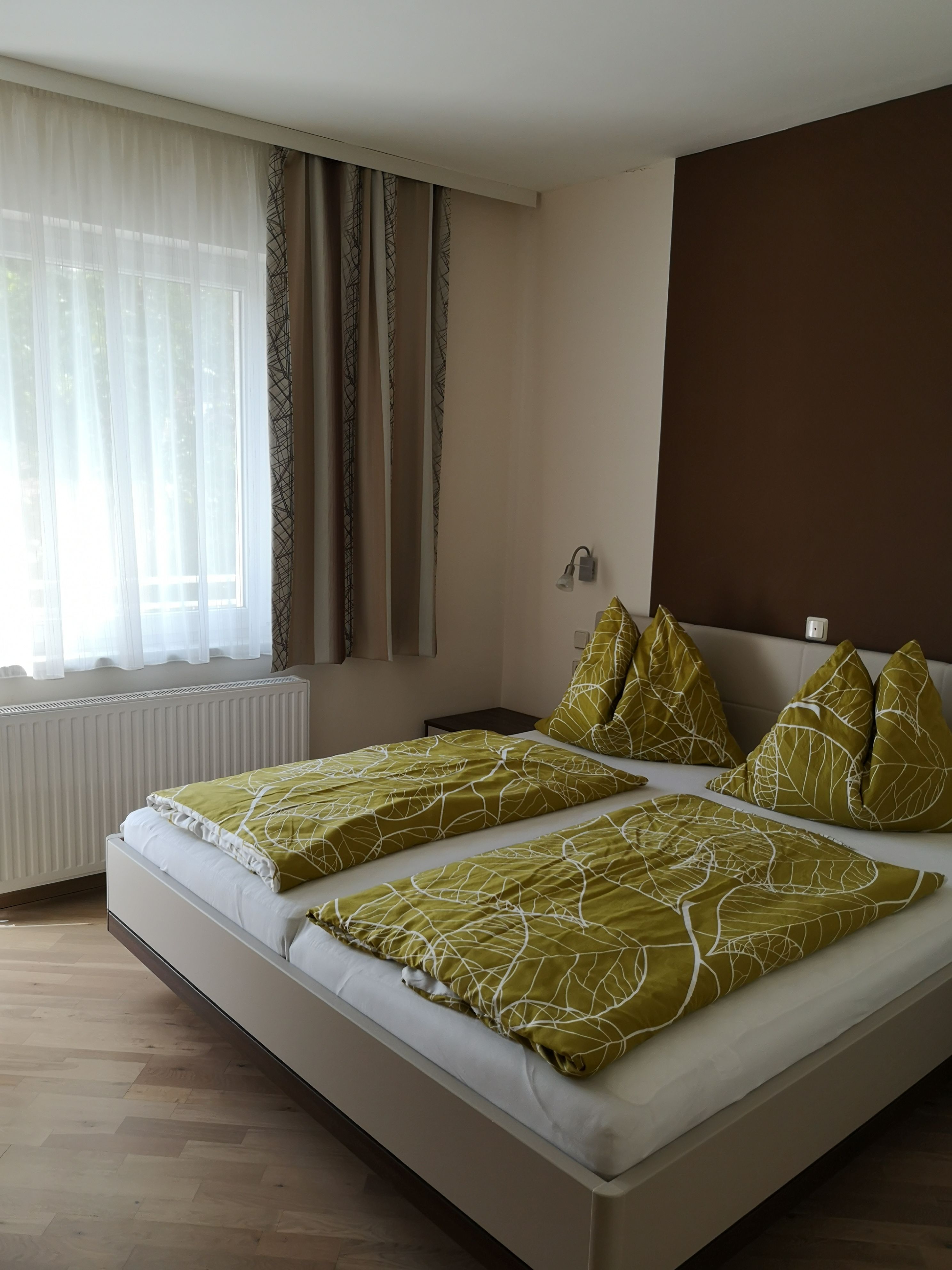 Dvoulůžkový pokoj s manželskou postelí, zeleným ložním prádlem a oknem se závěsy.