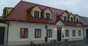 Dvoupodlažní budova se žlutou fasádou a červenou střechou.