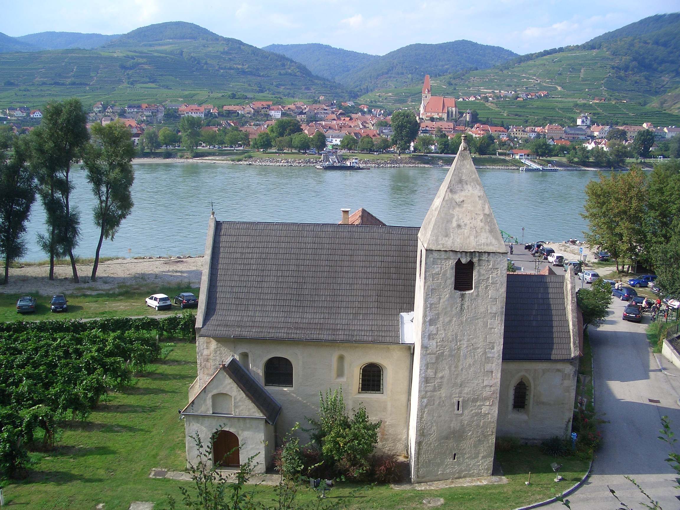 Kostel svatého Lorenze s řekou a vesnicí v pozadí.