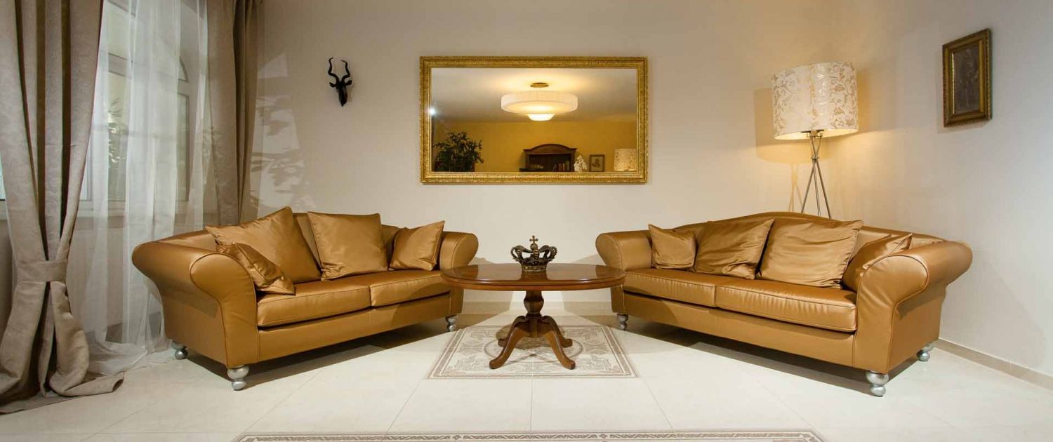 Elegantní vstupní hala se dvěma hnědými pohovkami, kulatým dřevěným stolem a velkým zrcadlem na stěně.